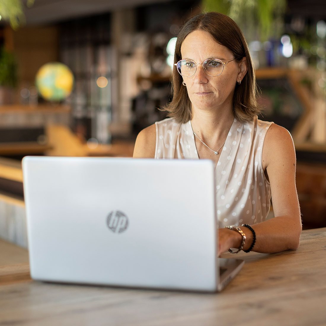 Manuela Hartmann sitzt mit Brille vor ihrem silbernen Laptop am Holztisch und bearbeitet die Webseite Datenschutzerklärung